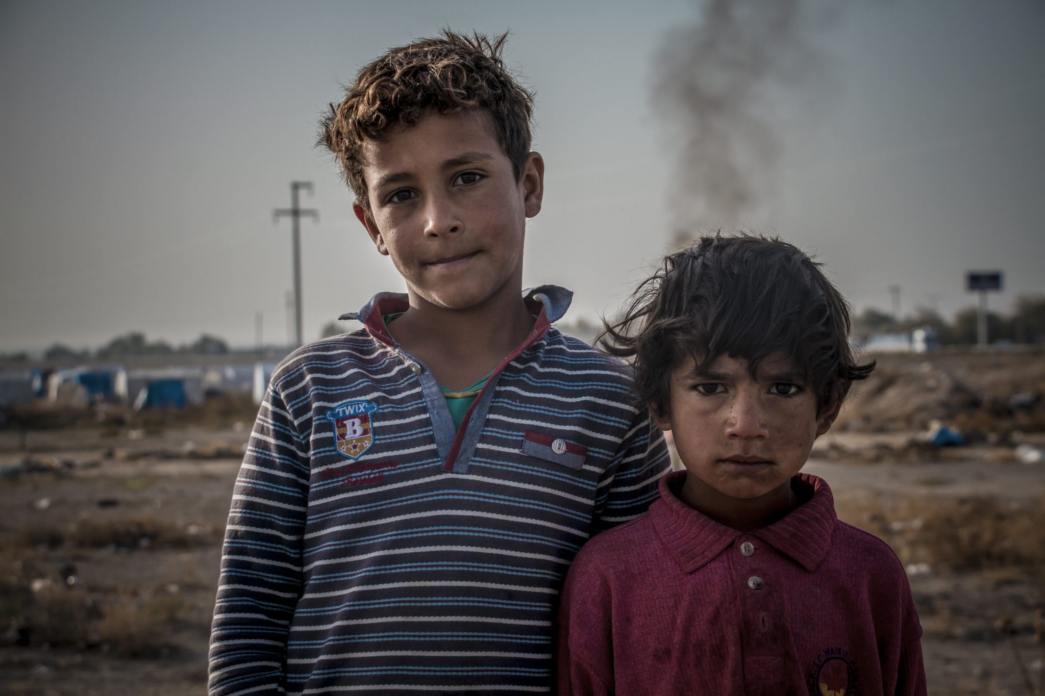 Två barn som är migranter i förgrunden. De ser trötta och nedstämda ut.